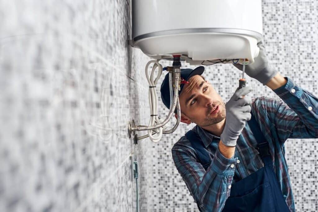Technician installing energy-efficient tank water heater with plumbing connections.